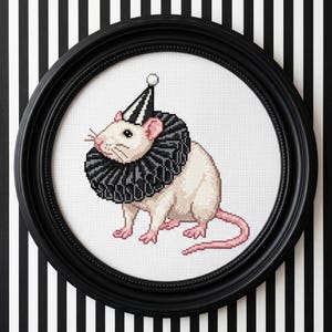 May include: A cross-stitch embroidery of a white rat wearing a black and white striped party hat and a large, pleated black ruff collar. The rat has pink ears, feet, and a long tail. The artwork is displayed in a round black frame.