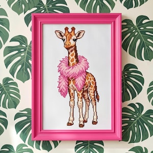 May include: A cross-stitch embroidery of a giraffe with a brown and white spotted pattern, wearing a fluffy pink feather boa around its neck. The artwork is displayed inside a bright, solid pink rectangular frame with a smooth finish.