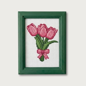 May include: A framed cross-stitch of a bouquet of pink tulips with green leaves and a pink bow. The artwork is set in a green wooden frame.