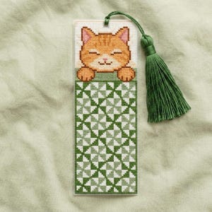 May include: A rectangular bookmark featuring a cross-stitched orange cat head at the top and a green and white geometric pinwheel pattern below. A green thread tassel is attached to the top center with a small loop of green embroidery floss.