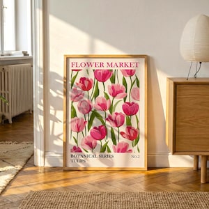 May include: A framed print with a floral design of pink tulips. The print is labelled "Flower Market" and "Botanical Series Tulips." The artwork is displayed in a room with a wooden cabinet, a woven basket, and a decorative lamp.