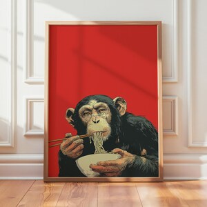 May include: A framed wall art print featuring a chimpanzee with dark fur eating noodles from a white bowl with wooden chopsticks against a solid, vibrant red background. The chimpanzee is depicted in a realistic style, holding the bowl with both hands.