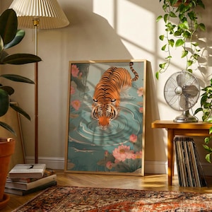 May include: A framed art print featuring a tiger in a pond with pink lotus flowers. The tiger has orange and black stripes. The water is teal. The artwork is displayed in a room with plants and a lamp.