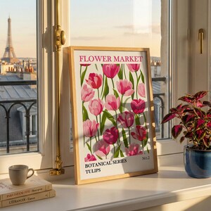 May include: A framed print with a floral design featuring pink tulips, labeled "FLOWER MARKET" and "BOTANICAL SERIES TULIPS." The print is displayed on a windowsill with a view of the Eiffel Tower and a small potted plant.