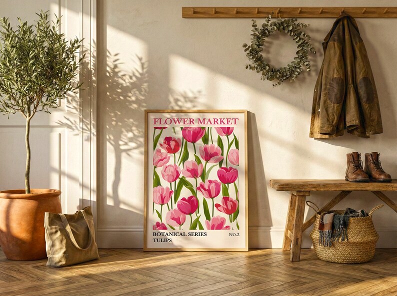 May include: A framed "Flower Market" poster featuring pink tulips with green stems and leaves. The poster is part of the "Botanical Series" and is displayed near a potted olive tree, a tote bag, and a wooden bench with a coat and boots.