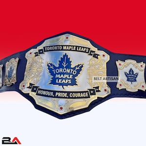 May include: A championship belt with a blue leather strap and gold and silver metal plates. The central plate features a blue maple leaf and the text "TORONTO MAPLE LEAFS". The words "HONOUR, PRIDE, COURAGE" are inscribed below.