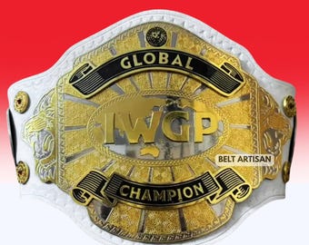May include: A white leather championship belt featuring a large gold and silver central plate with the text GLOBAL IWGP CHAMPION. The plate includes intricate engraved patterns, lion head side accents, and small gold circular studs along the strap.