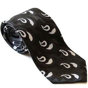May include: A necktie featuring a black base with a repeating pattern of white and grey paisley-inspired shapes. The fabric has a textured appearance with a woven finish, and the tie is rolled at the top, showing the pointed end at the bottom.