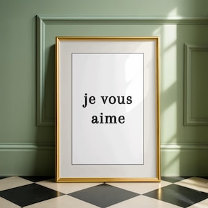 Puede incluir: Una impresión enmarcada con la frase francesa "je vous aime" en texto negro sobre un fondo blanco. El marco es dorado y la impresión se muestra contra una pared verde y un suelo a cuadros blanco y negro.