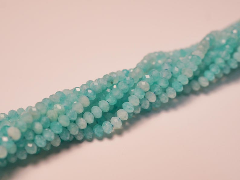 May include: Strand of faceted, round beads in shades of light blue and white. The beads are strung together, creating a textured, flowing appearance. The beads are likely made of a gemstone or glass, perfect for jewelry making.