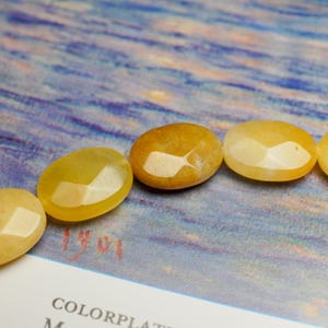 May include: Close-up of a strand of faceted, oval-shaped yellow beads. The beads have a polished, glossy finish and are arranged in a row. The background is a blue and white abstract design.