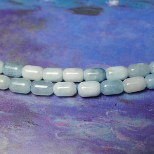 May include: Two strands of aquamarine gemstone beads. The beads are a mix of pale blue and white, with a smooth, rounded shape. The background is a textured blend of blue and purple.