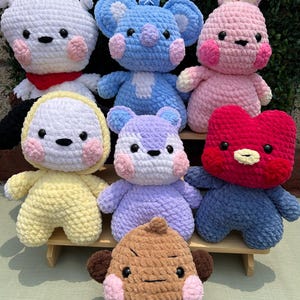 May include: A collection of handmade crochet plushies in various colors, including white, blue, pink, yellow, purple, red, and brown. Each plushie has a unique animal or character design with black eyes and pink cheeks. The text "@mo.crochet.space" is visible.