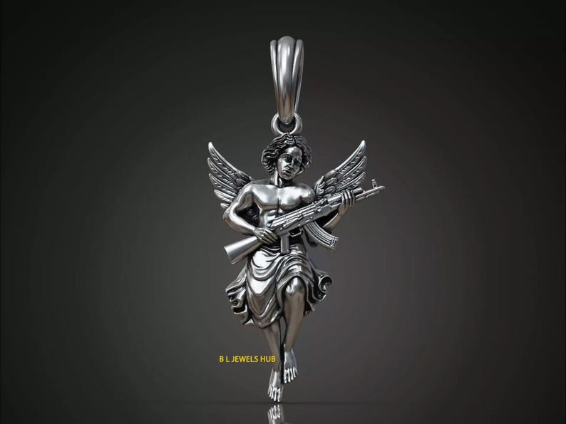 Puede incluir: Colgante de plata que representa un &aacute;ngel con alas, sosteniendo un rifle de asalto. El &aacute;ngel est&aacute; esculpido con detalle, en una pose cl&aacute;sica. El colgante tiene un lazo para una cadena. El texto "B.L. JEWELS HUB" est&aacute; en la parte inferior.