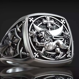 Könnte beinhalten: Ein silberner Ring mit detailliertem Design. Der Ring zeigt einen Löwen, der einen Stern, ein Kreuz und andere dekorative Elemente hält. Der Ring hat eine quadratische Oberfläche und ein detailliertes Band.