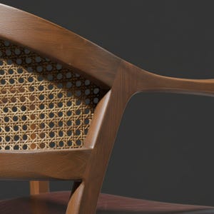 Pode incluir: Close-up de uma cadeira de madeira com encosto de palhinha. A estrutura da cadeira &eacute; castanha quente, e o encosto tecido &eacute; de cor bege claro. O design apresenta apoios de bra&ccedil;os curvos e uma constru&ccedil;&atilde;o robusta.