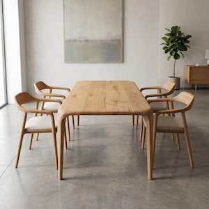 May include: A light oak dining table with a rectangular top and rounded corners, surrounded by four matching chairs. The chairs have curved backs and light-colored seats. The room has a neutral colour scheme.