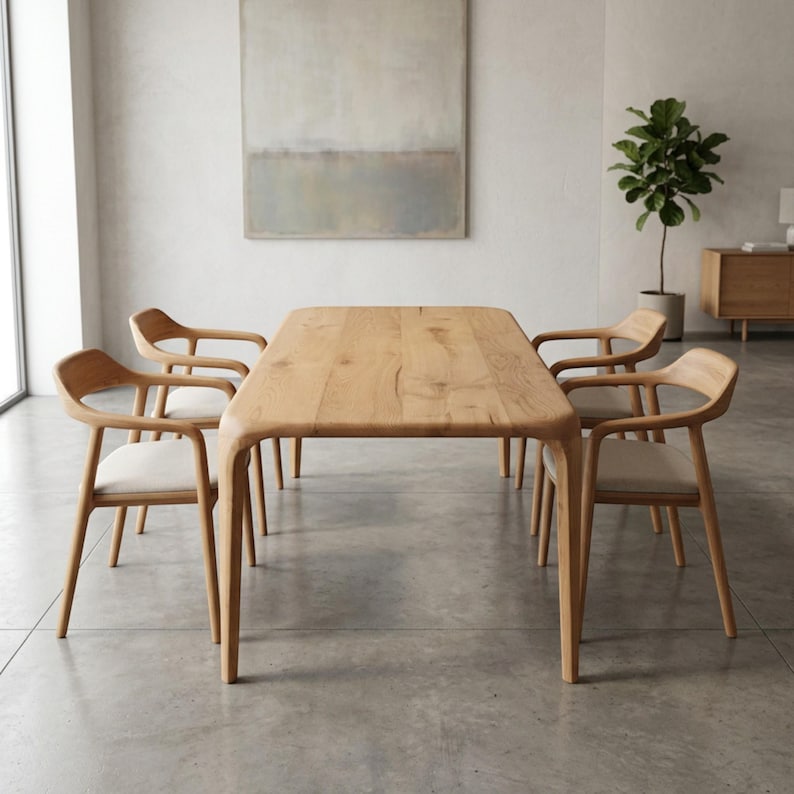 May include: A light oak dining table with a rectangular top and rounded corners, surrounded by four matching chairs. The chairs have curved backs and light-colored seats. The room has a neutral colour scheme.