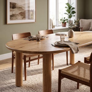 May include: An oval light wood dining table with thick cylindrical legs, surrounded by wooden chairs with woven seats. The table is set with ceramic plates, ribbed glass tumblers, metal cutlery, and beige linen napkins, plus a small ceramic vase.