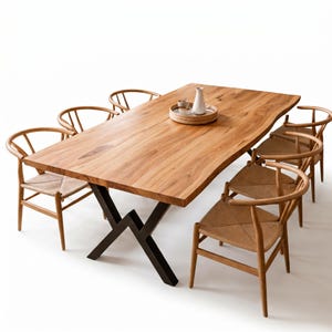 Op de afbeelding: Een houten eettafel met een natuurlijke rand en zwarte metalen poten, omringd door zes houten stoelen met geweven zittingen. Een dienblad met een vaas en kopjes staat op de tafel. De tafel is ongeveer 244 cm lang.