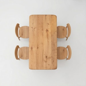 May include: An overhead shot of a light brown wooden dining table with rounded corners and four matching chairs. The table and chairs are made of light-coloured wood, showing the natural grain. The chairs have curved backs and circular seats.