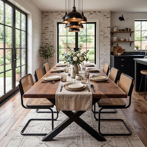 Peut inclure: Une salle à manger avec une longue table en bois foncé, dressée pour un repas. La table est entourée de chaises à dossier en osier et garnie d'assiettes, de verres et de couverts. Un arrangement floral est au centre, sous des suspensions noires.
