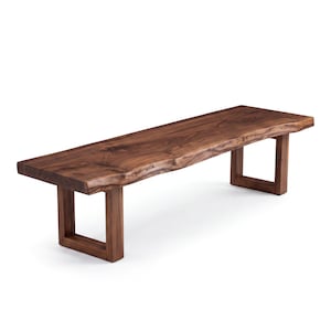 May include: A rectangular wooden bench featuring a natural live edge top with visible wood grain patterns in a deep brown tone. The bench is supported by two sturdy, U-shaped wooden legs that match the colour and finish of the seat surface.