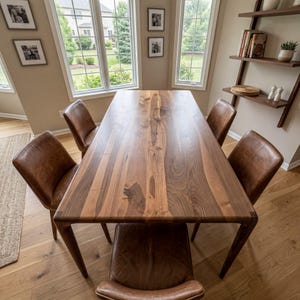 May include: A rectangular dining table made of dark brown wood with a visible grain pattern, featuring four matching chairs upholstered in brown leather. The table has a smooth, flat surface and four tapered legs, positioned in a room.