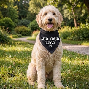 May include: A golden doodle dog sits in the grass, wearing a black bandana. The bandana has the text "ADD YOUR LOGO" in white, along with a paw print. The dog is in a park setting with green trees and grass.