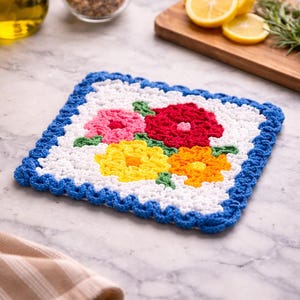 Può includere: Un sottopentola quadrato fatto a mano all'uncinetto con un motivo floreale. I fiori sono nelle tonalità del rosa, del rosso, del giallo e dell'arancione, con foglie verdi. Il bordo è blu brillante e lo sfondo è bianco. Questo oggetto decorativo è perfetto per la cucina.