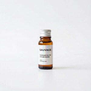 May include: A small amber glass bottle with a silver cap. The label reads "SAUVAGE FRAGRANCE OIL FOR PERFUME MAKING 20 ML HOSAGE %20". The bottle is filled with a clear, golden liquid. The background is plain white.