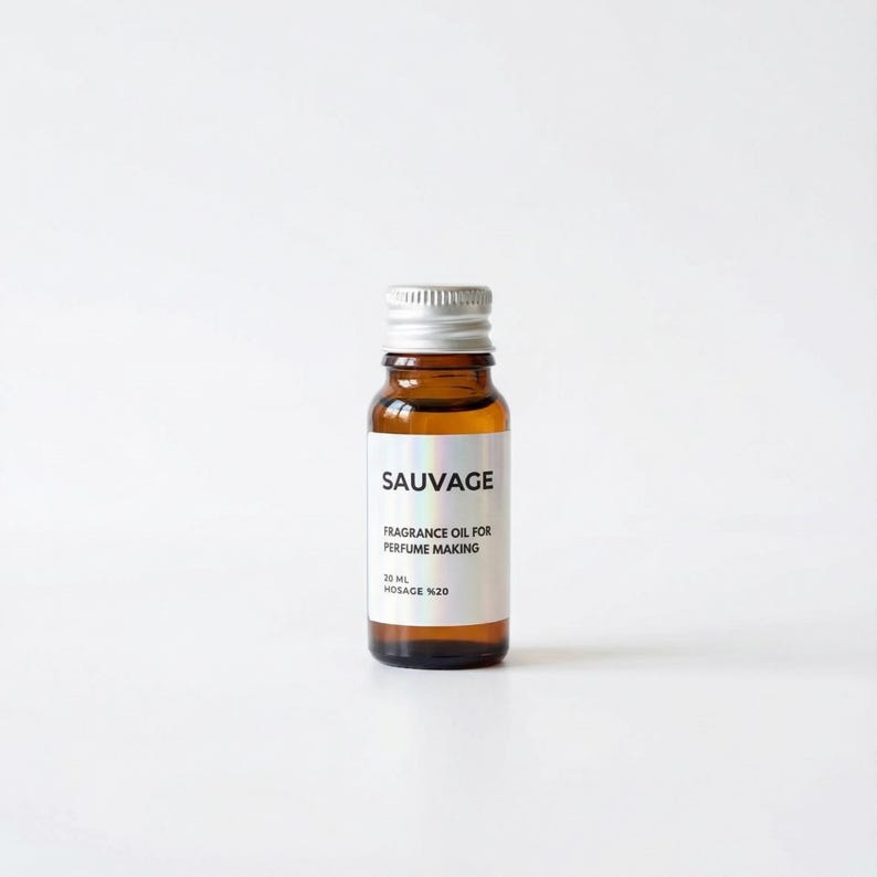 May include: A small amber glass bottle with a silver cap. The label reads "SAUVAGE FRAGRANCE OIL FOR PERFUME MAKING 20 ML HOSAGE %20". The bottle is filled with a clear, golden liquid. The background is plain white.