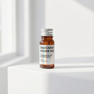 May include: A small, amber-colored glass bottle with a silver cap. The label reads "BACCARAT ROUGE 540" and "FRAGRANCE OIL FOR PERFUME MAKING." The bottle is filled with a clear liquid and sits on a white surface. The dosage is 20%.