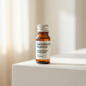 May include: A small, brown glass bottle with a silver cap, labeled "Yum Pistachio Gelato 33." The label also reads "Fragrance Oil for Perfume Making" and lists the volume as 10 ml. The bottle is positioned on a white surface.