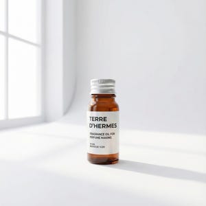 May include: A small brown glass bottle with a silver cap, labeled "TERRE D'HERMES FRAGRANCE OIL FOR PERFUME MAKING." The label also indicates a 10 ml volume. The bottle is set against a white background with soft lighting.