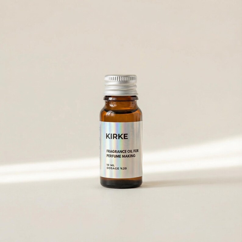 May include: A small, brown glass bottle with a silver cap. The label reads "KIRKE FRAGRANCE OIL FOR PERFUME MAKING 10 ML DOSAGE %20". The bottle is filled with a clear liquid and sits against a neutral background.