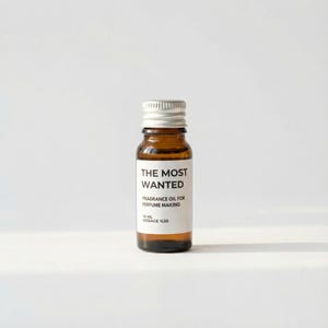 May include: A small amber glass bottle with a silver cap. The bottle has a white label with the text "THE MOST WANTED" and "FRAGRANCE OIL FOR PERFUME MAKING". The bottle contains 10 ml of fragrance oil with a dosage of 20%.
