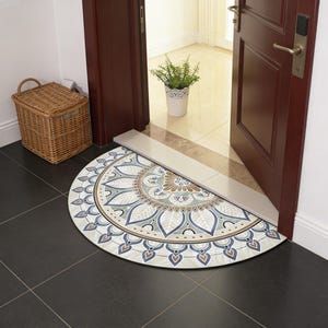 Puede incluir: Una alfombra de media luna con un diseño de mandala detallado en tonos azules, marrones y crema. La alfombra está colocada en una puerta, con una cesta de mimbre y una planta en maceta en el fondo. El diámetro de la alfombra es de aproximadamente 76 cm.