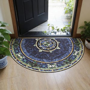 Puede incluir: Una alfombra de media luna con un diseño de mosaico. La alfombra presenta un fondo azul oscuro con un patrón circular en el centro, acentuado con detalles verdes, blancos y dorados. La alfombra está colocada frente a una puerta negra.