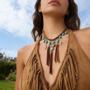 May include: A brown suede necklace with turquoise beads and silver feather charms. The necklace has brown suede tassels and is worn with a brown suede top with fringe.