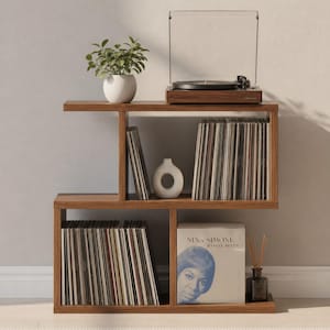 Puede incluir: Un mueble de madera para tocadiscos con un tocadiscos, discos de vinilo y objetos decorativos. El mueble es de madera marrón y tiene varios estantes. También se ven un jarrón blanco, una pequeña planta en maceta y un frasco de difusor de caña.