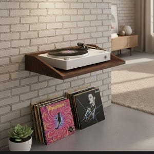 May include: A white turntable with a black record sits on a dark brown wooden shelf mounted on a brick wall. Below, a collection of vinyl records is displayed, including album covers with colorful designs and a jazz portrait. A small potted succulent is also visible.