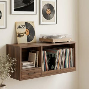 May include: A dark brown floating media console with a drawer, open shelving, and a turntable. The console holds vinyl records, books, and a record player. Framed vintage record art hangs above the console. The album cover reads "JAZZ".