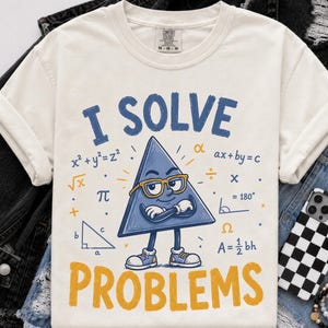 May include: An ivory short-sleeve t-shirt featuring a blue cartoon triangle character wearing yellow glasses with arms crossed. The text reads I SOLVE PROBLEMS, surrounded by mathematical formulas including x squared plus y squared equals z squared.