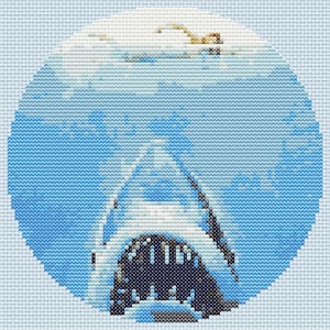 May include: Cross-stitch artwork featuring a shark's open mouth with visible teeth, set against a blue and white ocean background. The design is circular, with varying shades of blue and white thread creating the image.