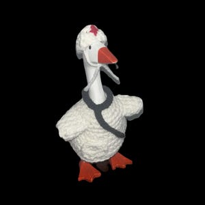 May include: A white goose figurine wearing a white hat with a red star, a grey stethoscope, and orange feet. The goose is made of a textured, knitted material and has an orange beak. The background is black.