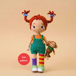 May include: Crocheted doll with red hair in two braids, wearing an orange top, green dungarees, and striped socks. The doll holds a brown crocheted monkey. The doll is wearing green and white trainers. A red circle with the text "PDF pattern" is in the image.