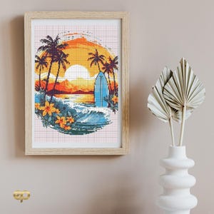 May include: Framed cross-stitch art depicting a sunset beach scene with palm trees, a surfboard, and ocean waves. The artwork features a vibrant color palette of orange, yellow, blue, and green, and is encased in a light brown wooden frame.