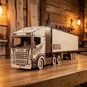 Pode incluir: Um caminhão de brinquedo de madeira com uma cabine Scania com detalhes cortados a laser e um reboque com o texto Maral. O veículo é construído com painéis de madeira clara e escura, exibindo uma grade detalhada, rodas e padrões laterais.