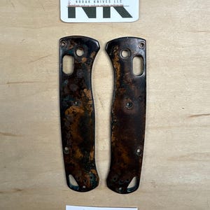 May include: Two brown knife handle scales with a distressed finish and copper-colored accents. The scales have holes for screws and a curved shape. A label reads "Coffee Grind". A business card with the logo "NK" is at the top.